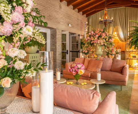 A cozy, elegant living room decorated with pink sofas, large floral arrangements, candles in glass holders, and soft lighting, creating a warm and inviting atmosphere with a touch of luxury.